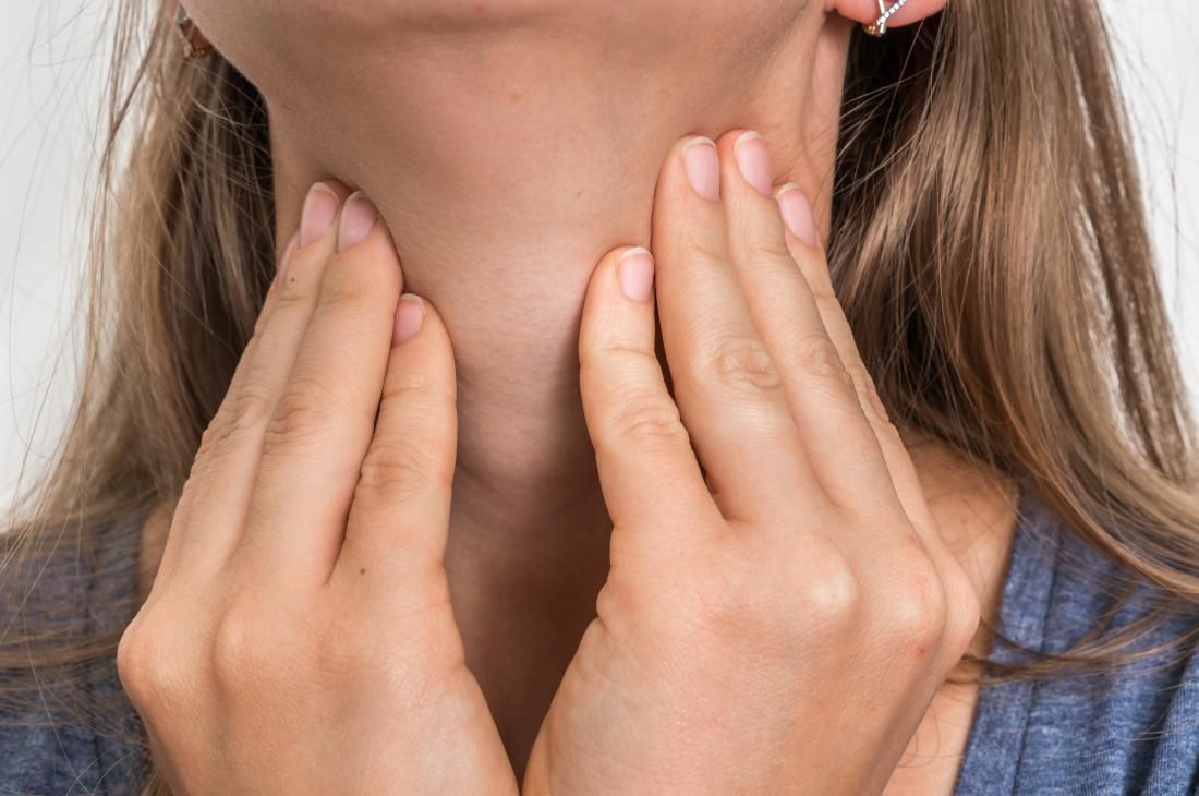 Close-up of a woman with her fingers gently pressing against her throat around the location of the thyroid gland