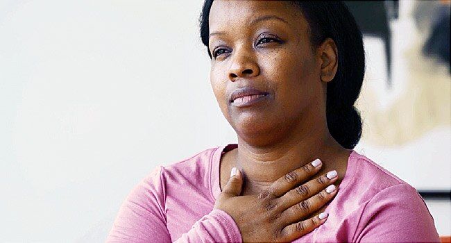 Woman looking uncomfortable as she holds her hand against her neck under the thyroid gland