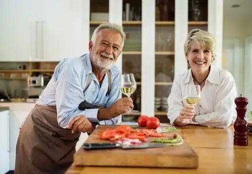 an older couple standing near food in the kitchen