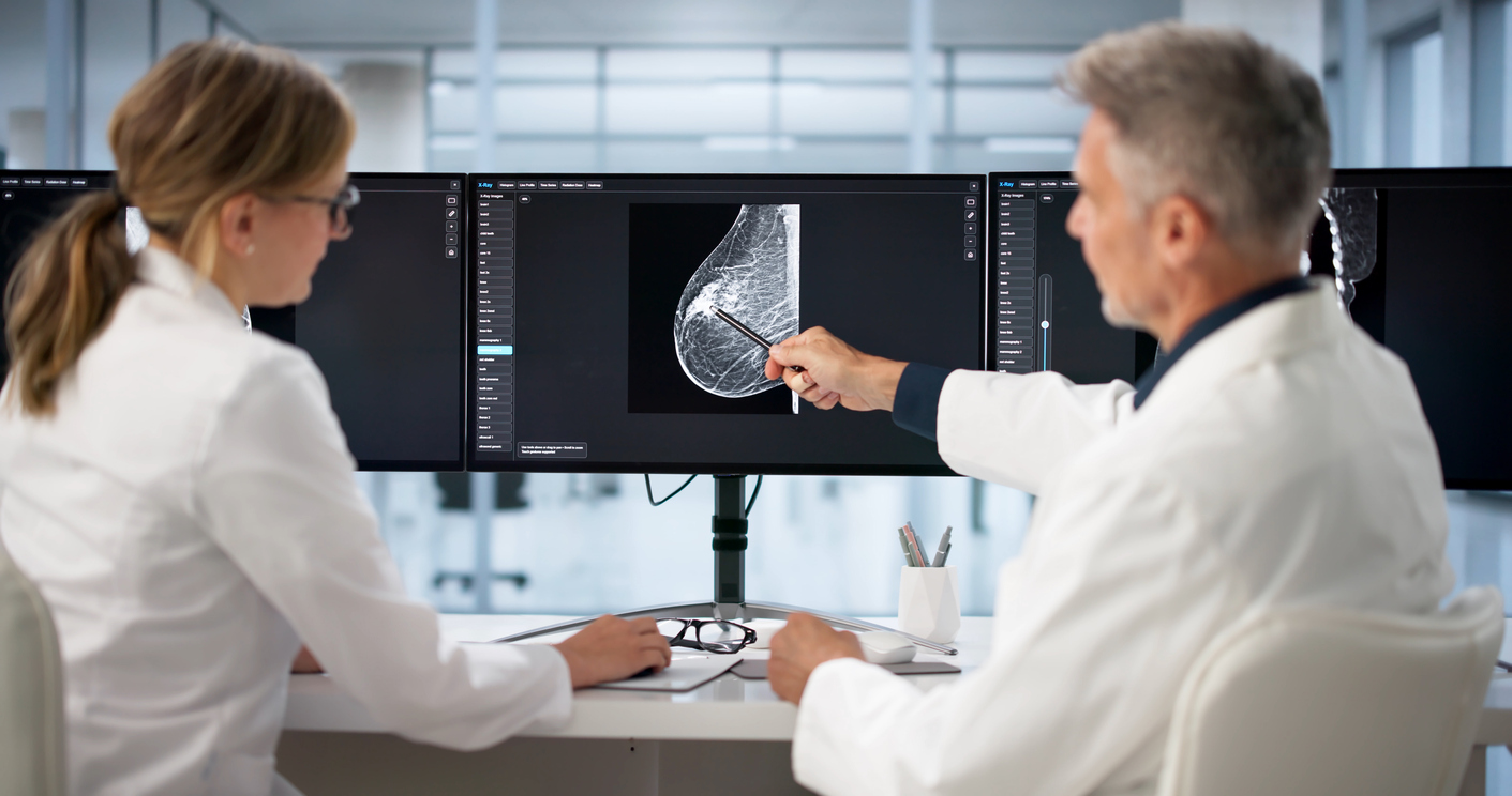 Two doctors reviewing a mammogram image on a computer screen in a medical office setting