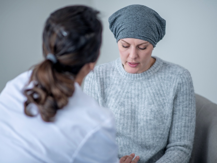 Female patient wearing a gray headscarf talks to a doctor in a white coat in a clinical setting.