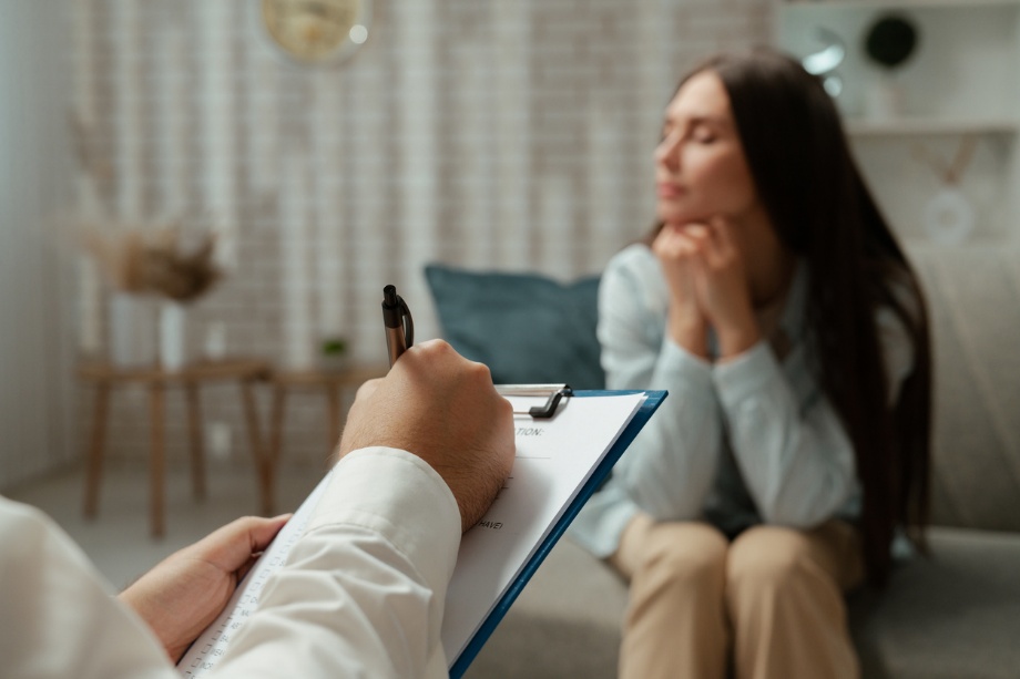 Therapist taking notes while a woman sits on a couch during a counseling session in a cozy room.