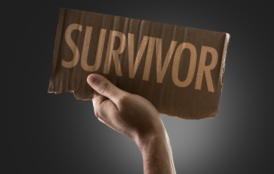 Hand holding torn cardboard with the word SURVIVOR in bold letters against a dark background