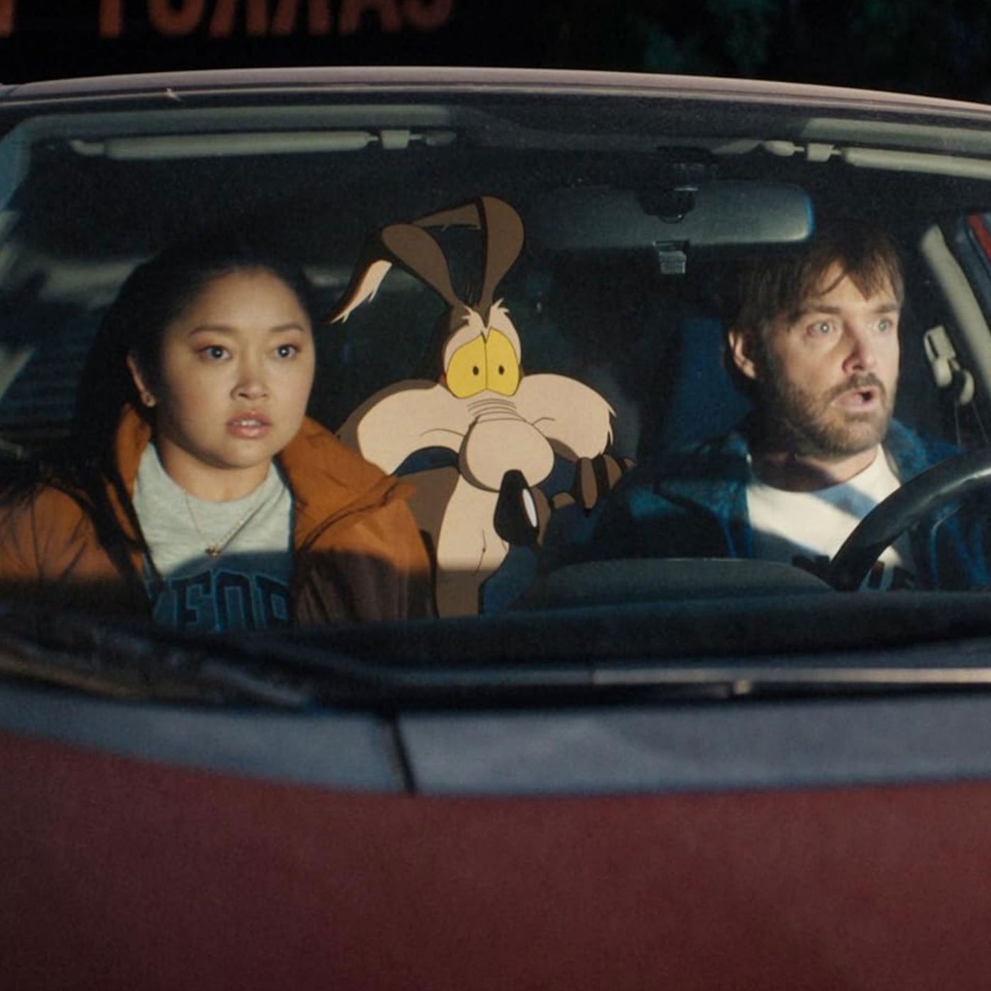 Two people and an animated cartoon coyote sitting in a car at night with surprised expressions.