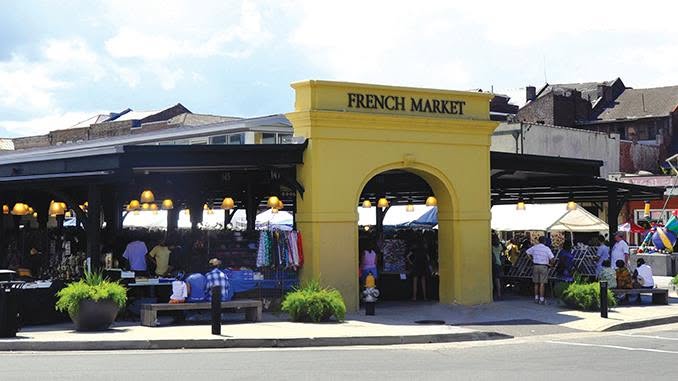 Yellow entrance arch to the French Market with people shopping under covered stalls on a sunny day.