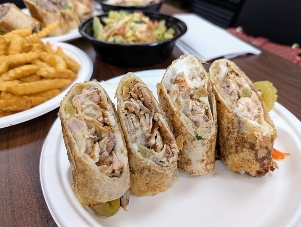 Grilled chicken wraps cut in halves served on a white plate with crinkle fries and salad in the background