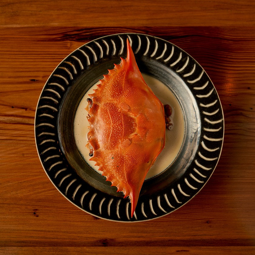 Top view of a cooked crab with an orange shell served on a black decorative plate on a wooden table.