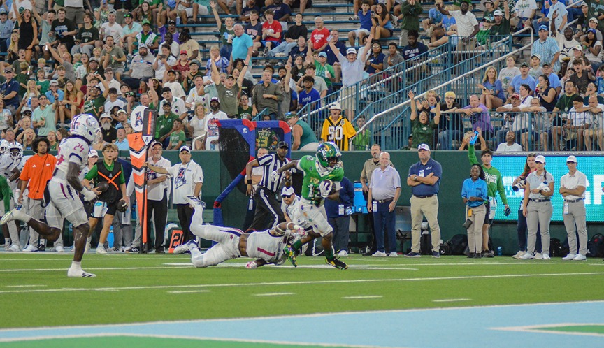 Football player in green uniform evades tackle during a game with a large crowd in the stadium stands