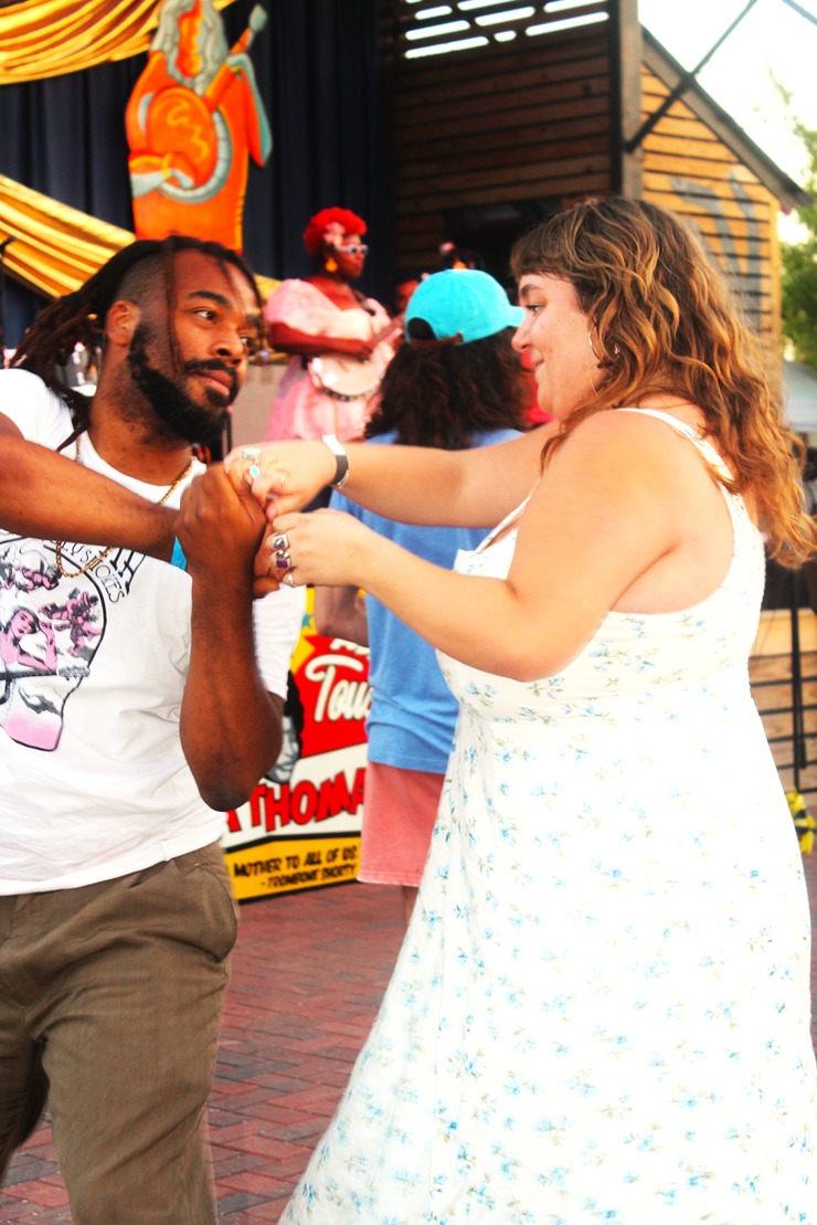 Man and woman dancing together outdoors at a lively event with musicians in the background.