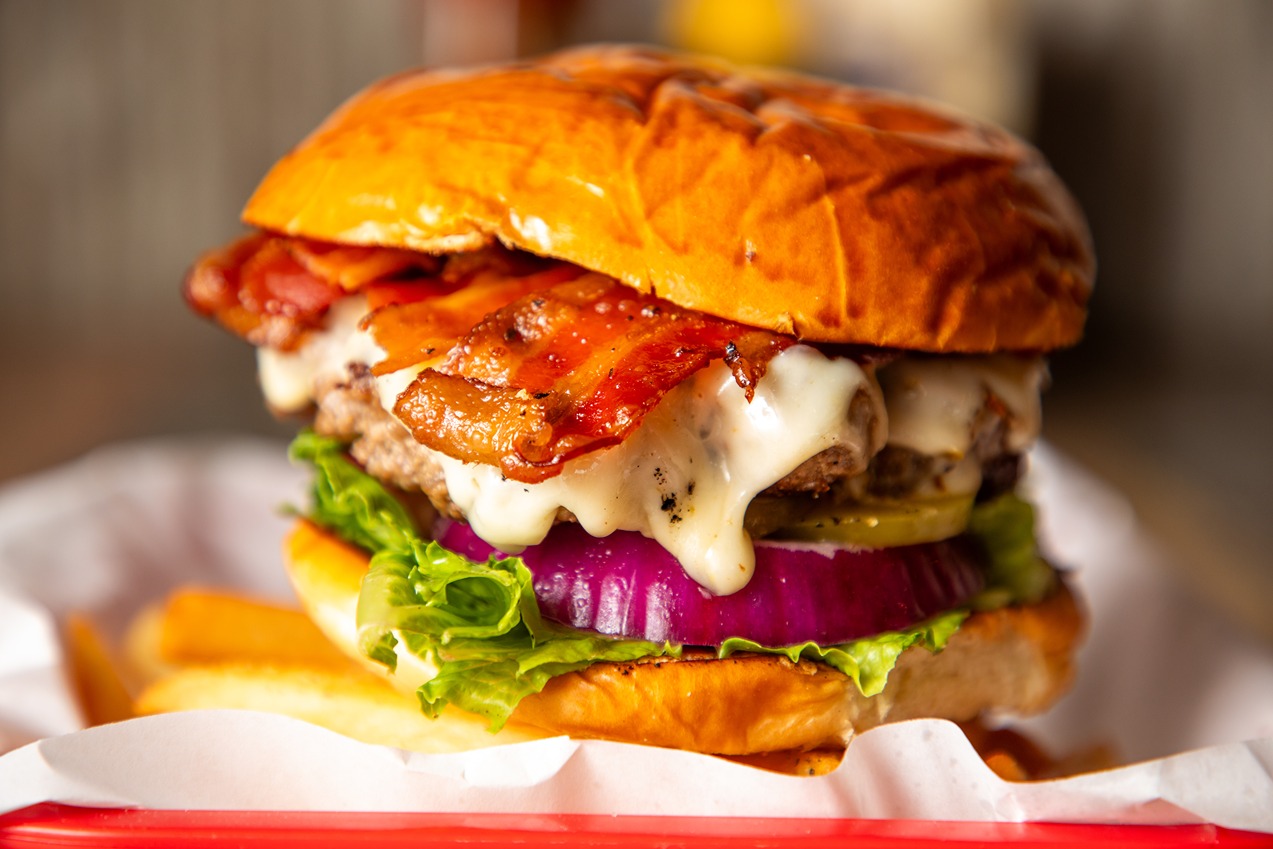 Close-up of a bacon cheeseburger with lettuce, red onion, pickles, melted cheese, and a toasted bun.