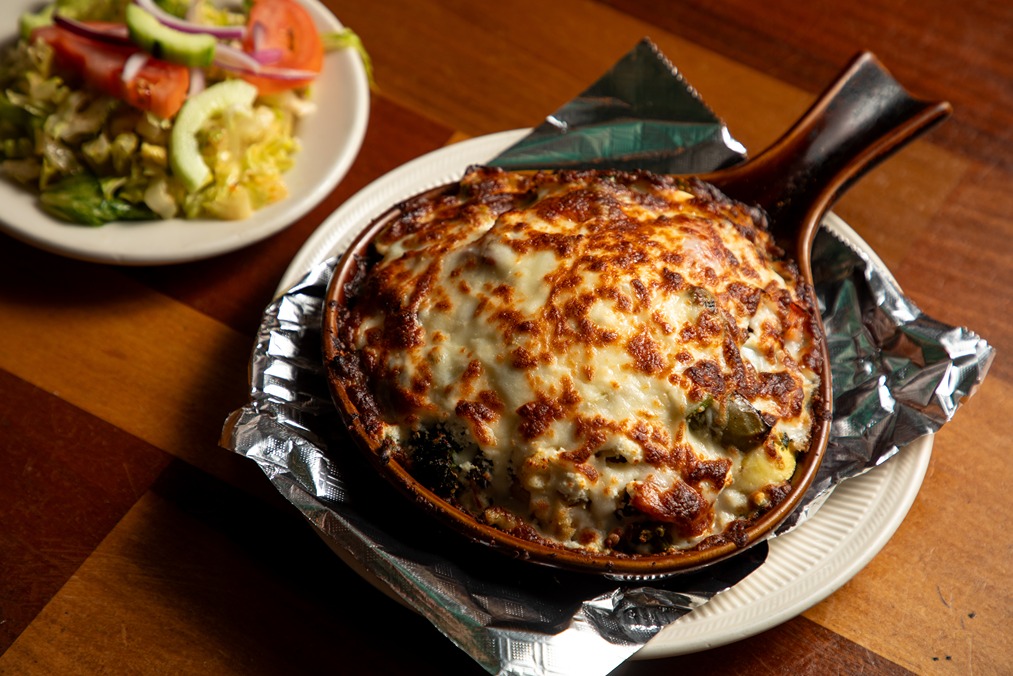 Baked casserole dish with golden melted cheese served on foil, alongside a fresh garden salad on a wooden table.