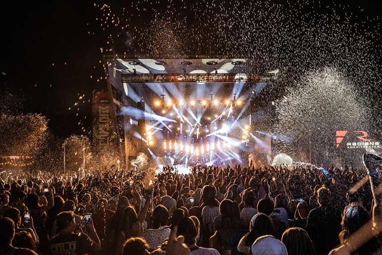 Crowd enjoying an outdoor concert with bright stage lights and confetti in the night atmosphere