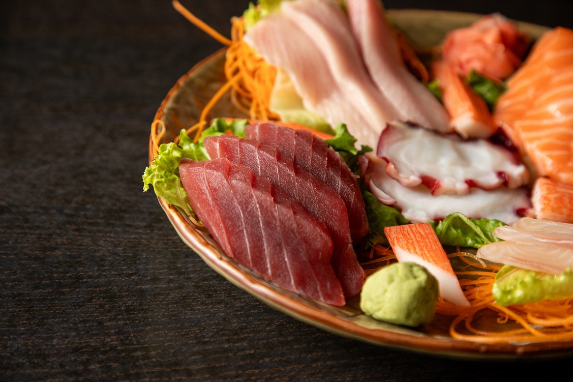 Plate of assorted sashimi including tuna, salmon, octopus, and wasabi on a ceramic dish with garnish.