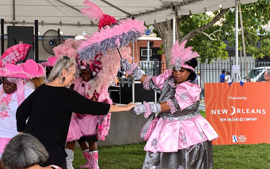 Woman in pink elaborate costume dancing with a spectator under a tent at New Orleans festival event.