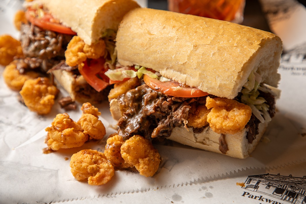 Po Boy sandwich with fried shrimp, roast beef, lettuce, and tomato on French bread with shrimp spilling out.