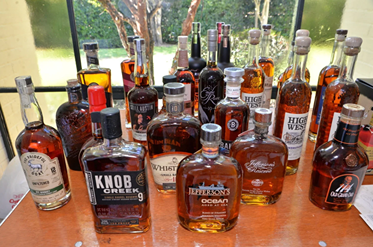 Variety of whiskey bottles including Knob Creek, Jefferson's, and High West displayed on a wooden table by a window.