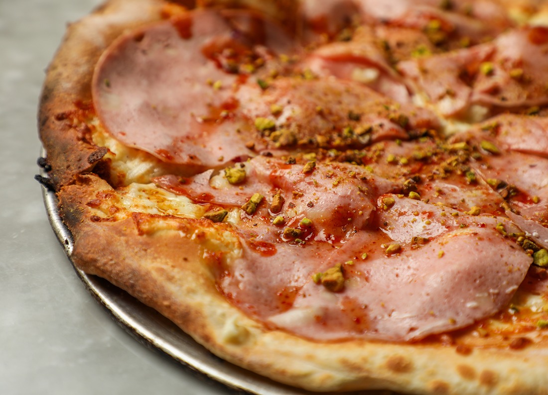 Close-up of a thin-crust pizza topped with slices of ham and sprinkled with crushed pistachios.