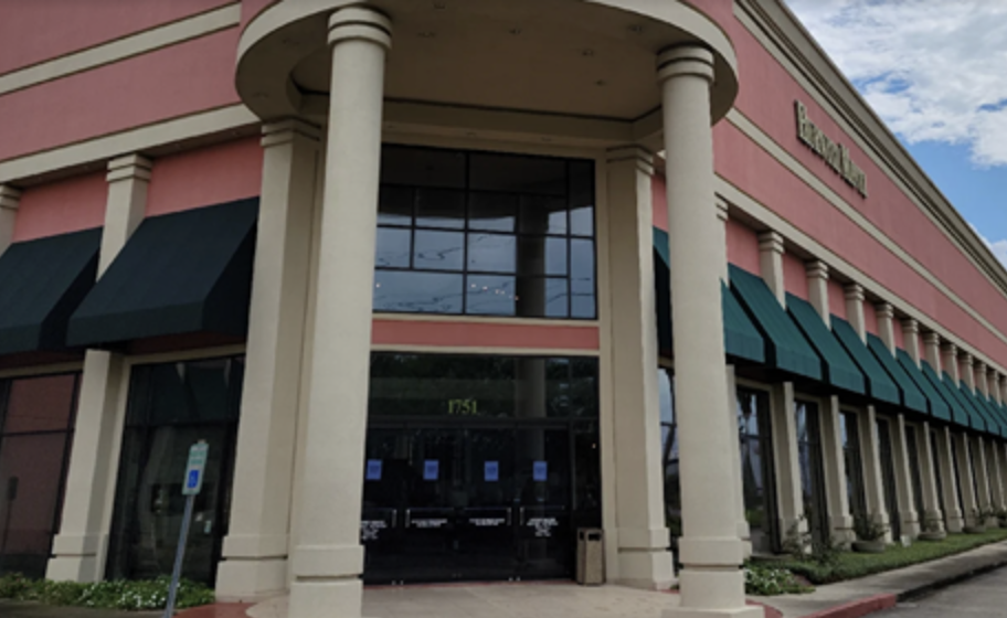 Exterior view of a large commercial building with tall white columns and green window awnings under a blue sky