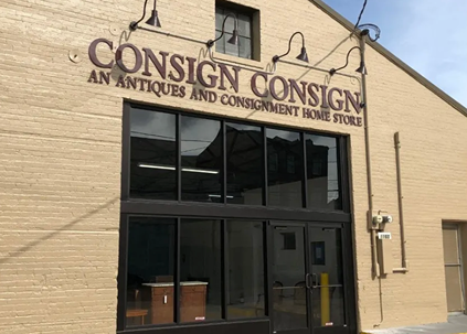 Storefront of Consign Consign antiques and consignment home store with large black glass door and beige brick wall
