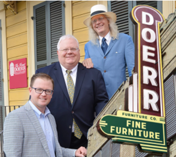 Three men in business attire posing outside Doerr Fine Furniture store with vintage signage on wooden building.
