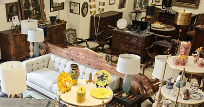 Vintage furniture and decorative antiques including sofas, lamps, plates, and wooden chests in a cozy room.