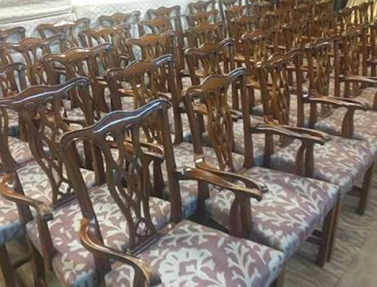 Rows of vintage wooden chairs with carved backs and patterned cushioned seats in a spacious room.