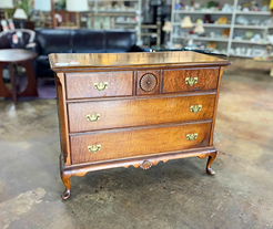 Antique wooden dresser with ornate brass handles and carved details on curved legs in a vintage store.