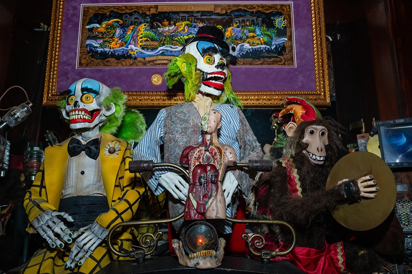 Three spooky puppets including clowns and a monkey playing cymbals, set against a colorful framed artwork background.