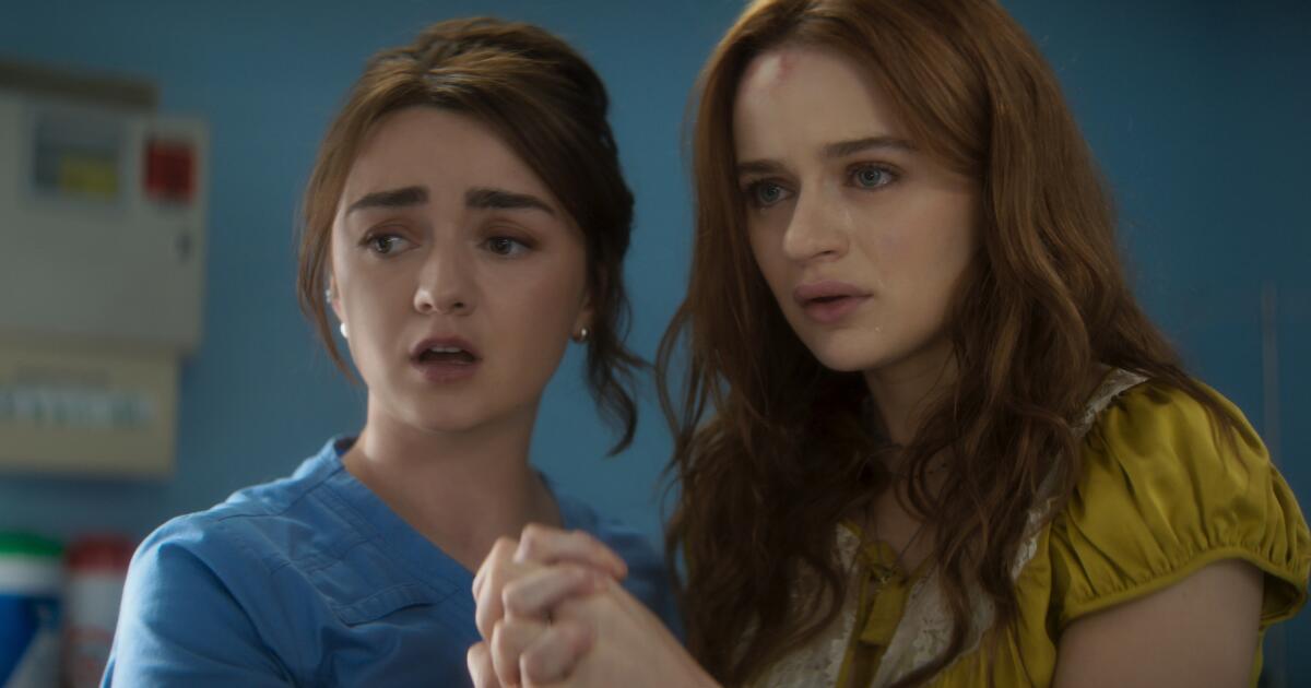 Two concerned women holding hands, one in blue scrubs and the other with a forehead injury in a yellow top.