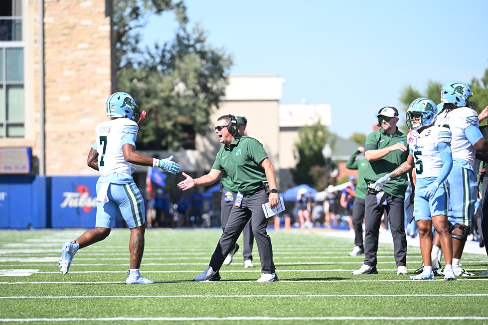Football coach reaches out to shake hands with player wearing number 7 on green turf field during game day.