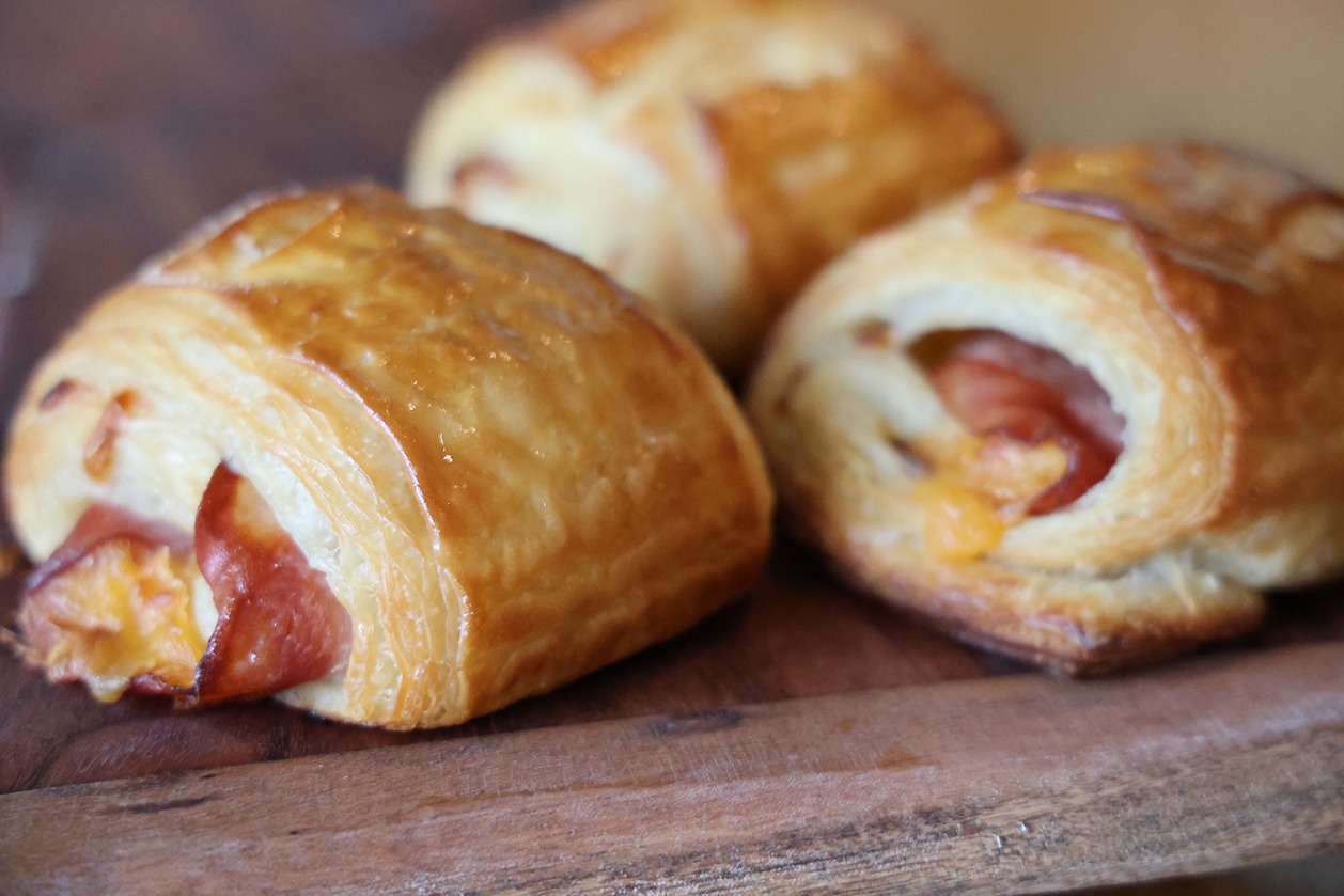 Three golden-brown ham and cheese puff pastries on a wooden cutting board close-up