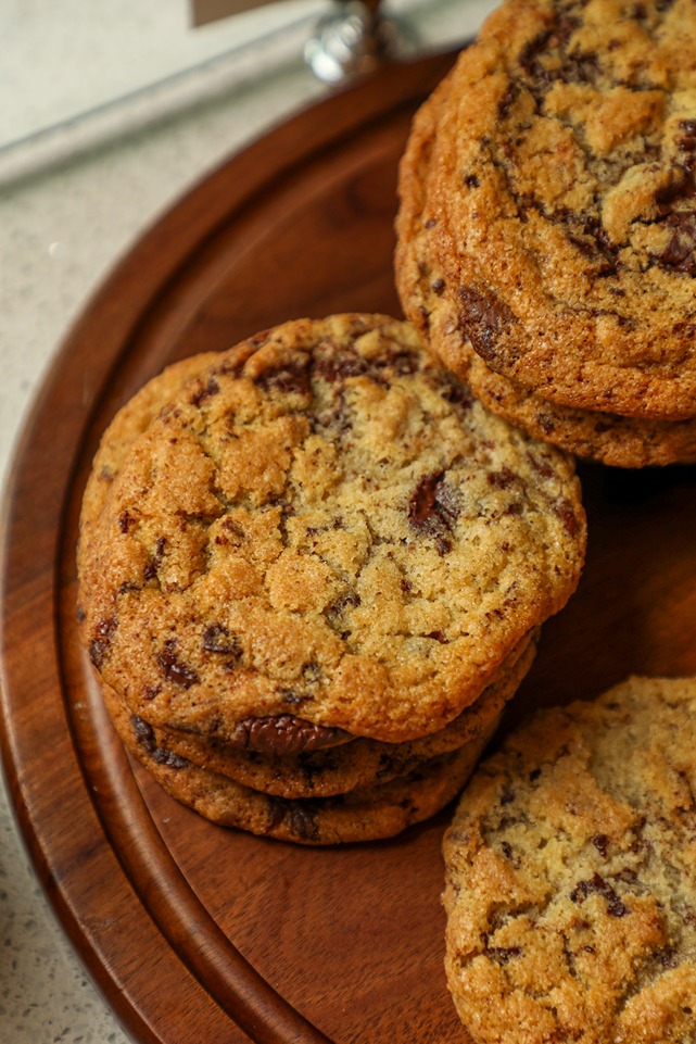 Close-up of freshly baked chocolate chip cookies stacked on a wooden serving plate.