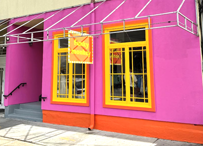 Vibrantly painted pink wall with orange trim and yellow-framed windows of Funky Monkey store under metal awning