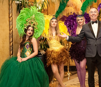 Performers in vibrant feathered costumes and a man in a tuxedo at an elegant event venue