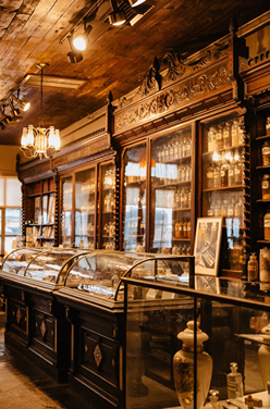 Interior of a vintage apothecary with wooden shelves, glass display cases, and antique bottles.