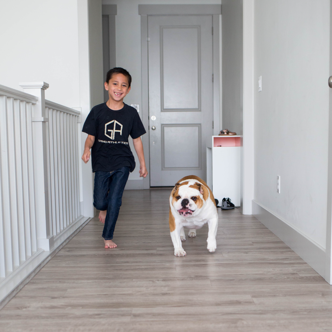 young boy and a pug dog running down a hallway on hardwood flooring
