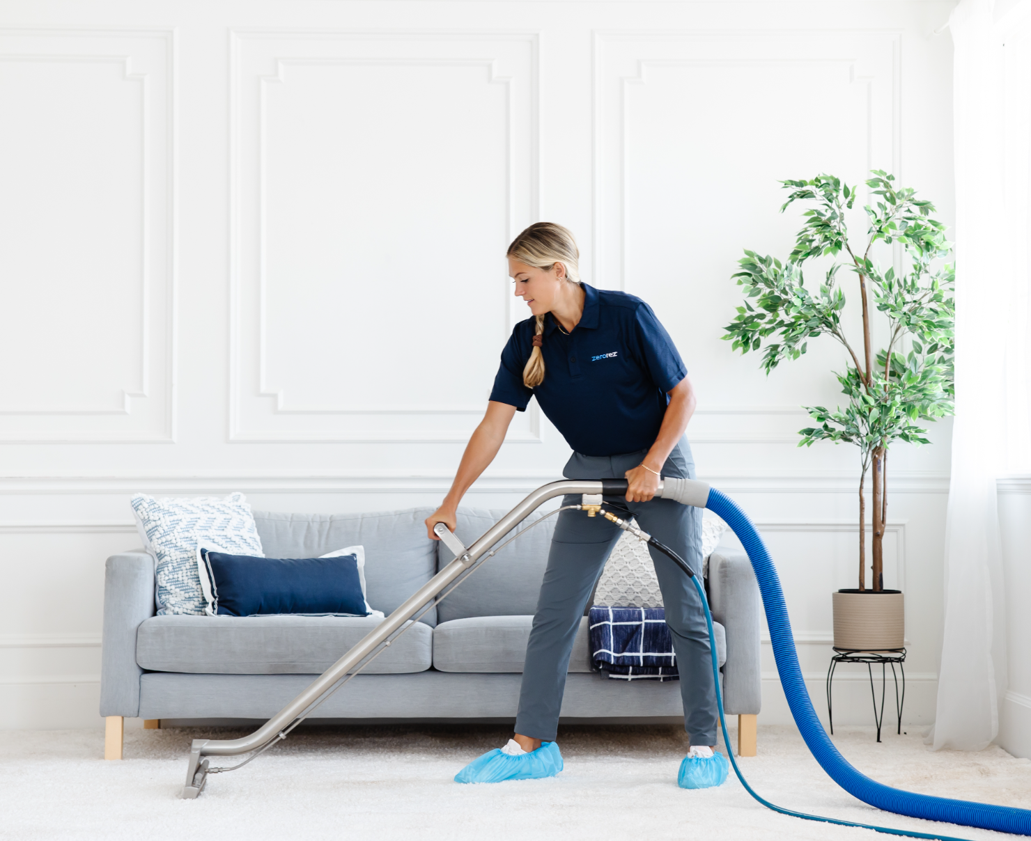 Zerorez female technician cleaning a living room with a Zr™ Wand, which extracts dirt and grime from a white carpet, leaving no sticky residue behind after cleaning