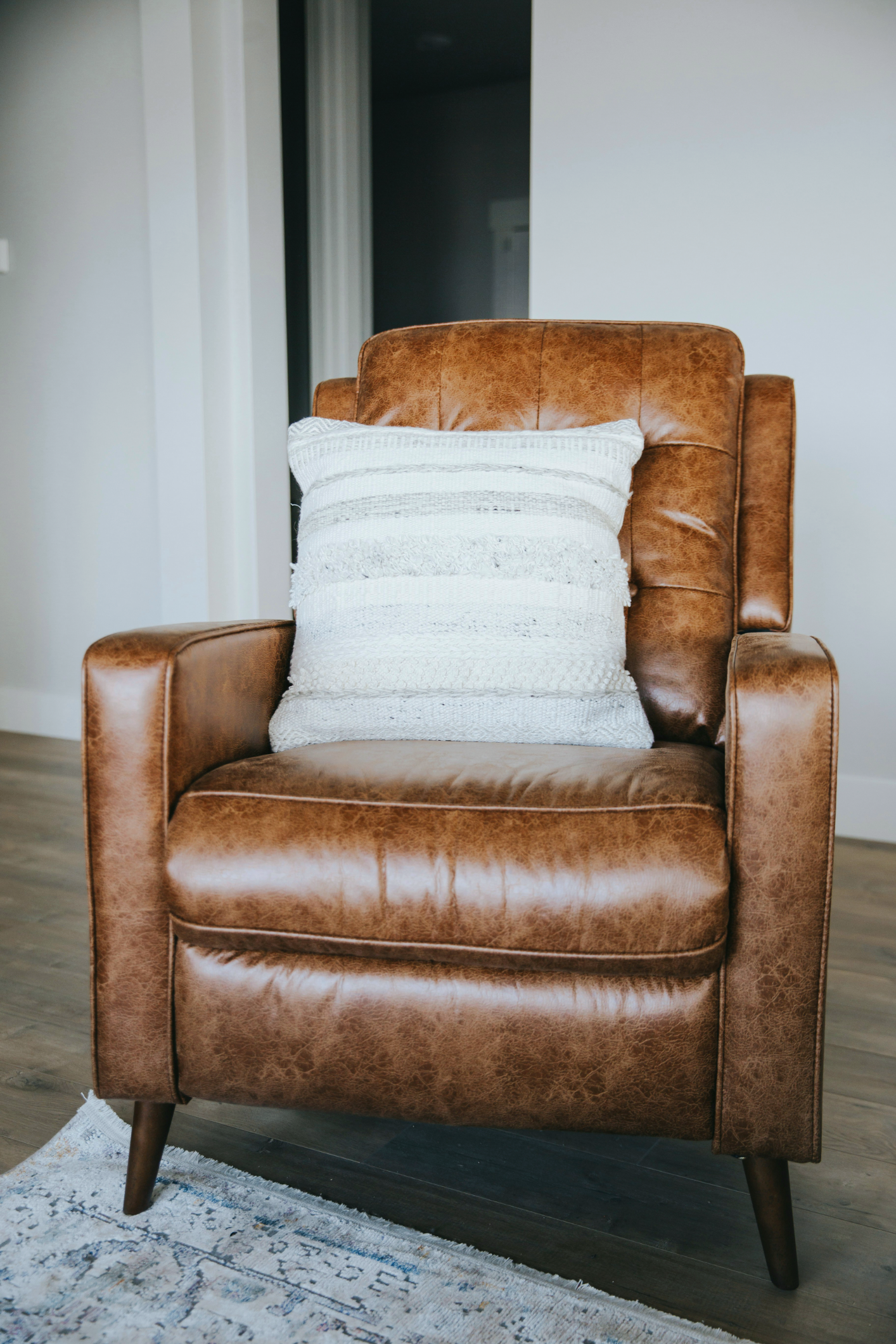 brown leather upright chair in a white room with a white and gray striped pillow sitting on it