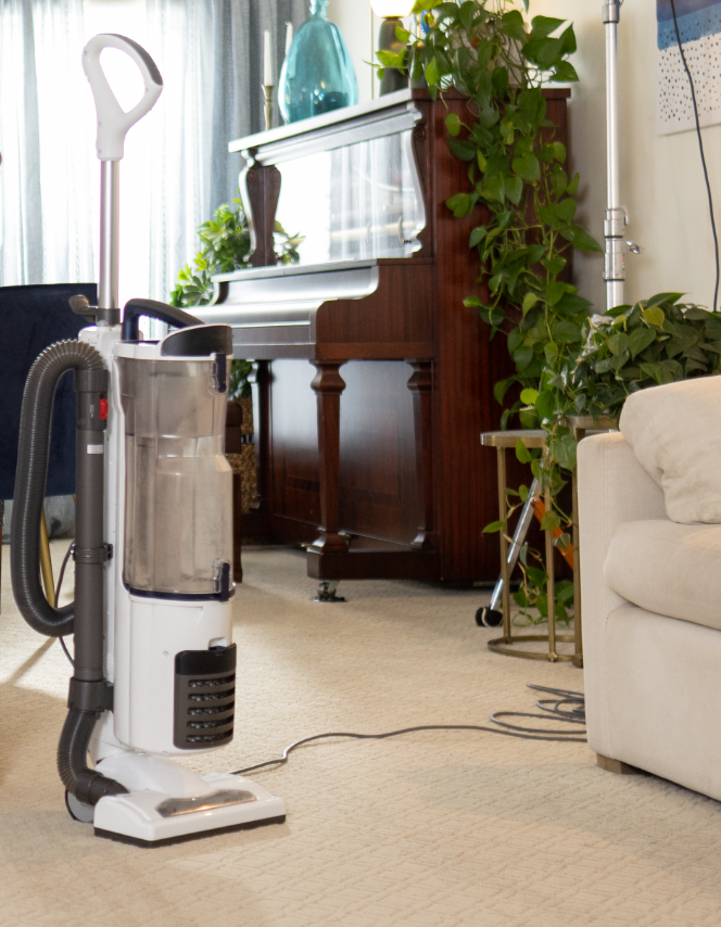 White upright vacuum, plugged in, and waiting to be used in a living room