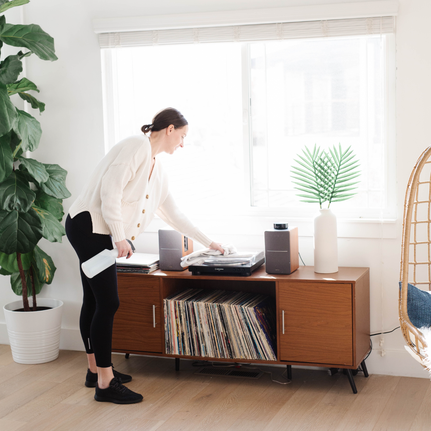 woman dusting a vinyl record player on a side table holding vinyl albums wondering how often to dust