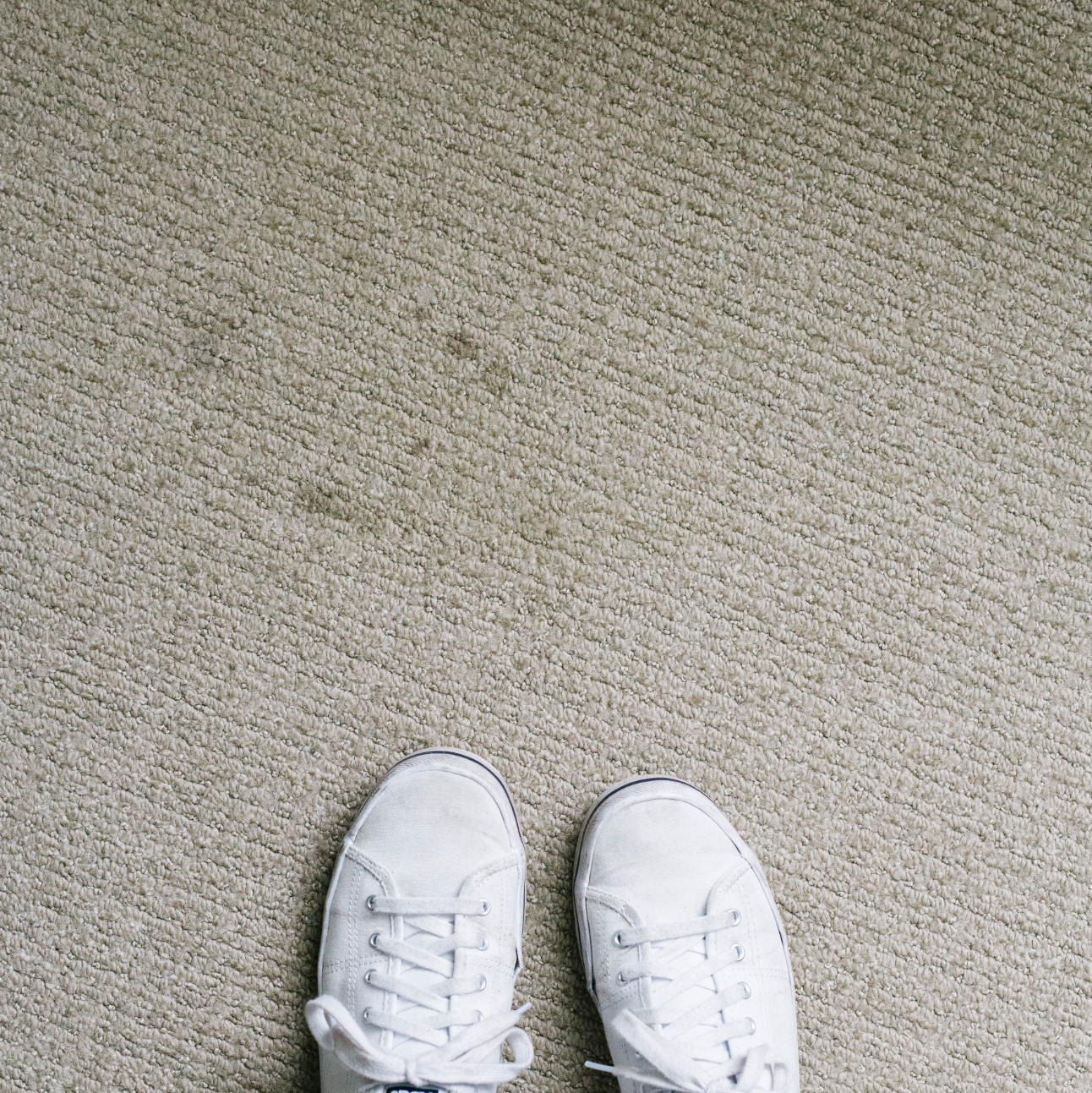 pair of white shoes on beige carpet with wicking stains