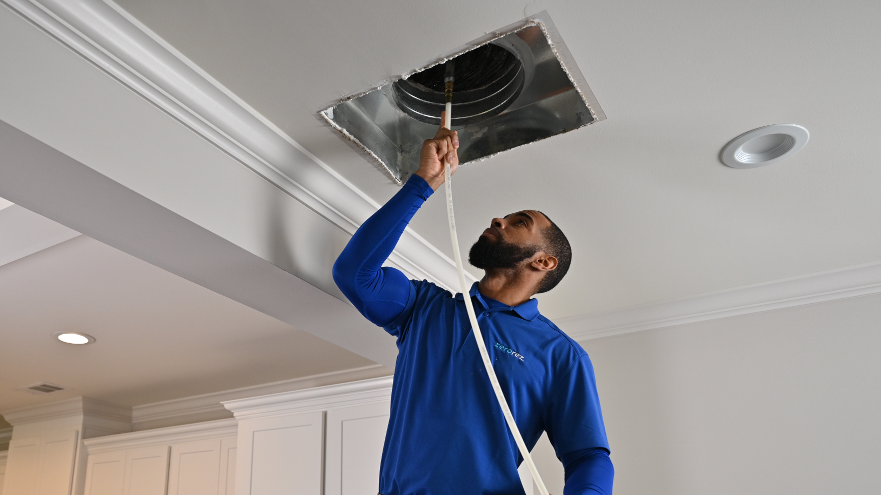 a male Zerorez technician cleaning out air ducts in the ceiling of a residential home in order to reduce allergy symptoms