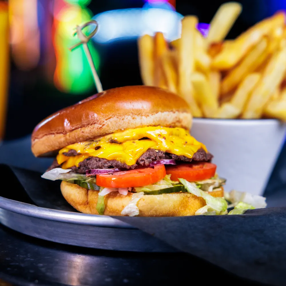 Cheeseburger with lettuce, tomato, onions, and pickles served on a plate with french fries in background.