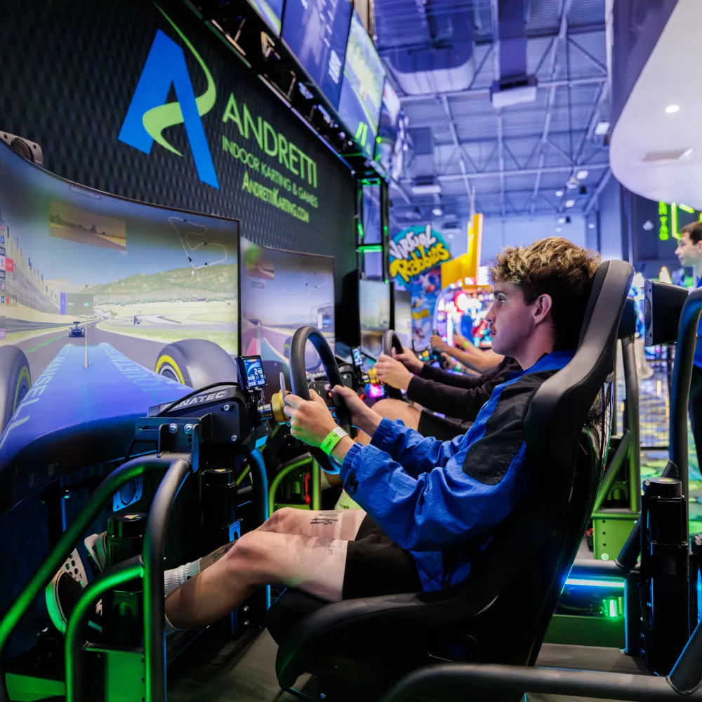 Young man focused on driving simulator at indoor gaming arcade with bright screens and neon lights