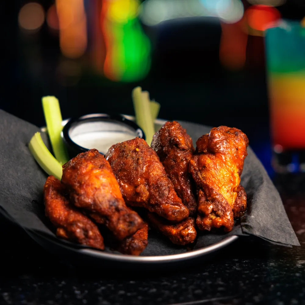 Spicy buffalo chicken wings served with celery sticks and ranch dipping sauce on a black plate.