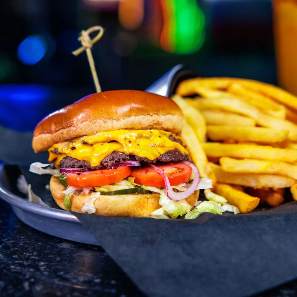 Cheeseburger with lettuce, tomato, onion, pickles, and melted cheddar paired with golden French fries on a plate.