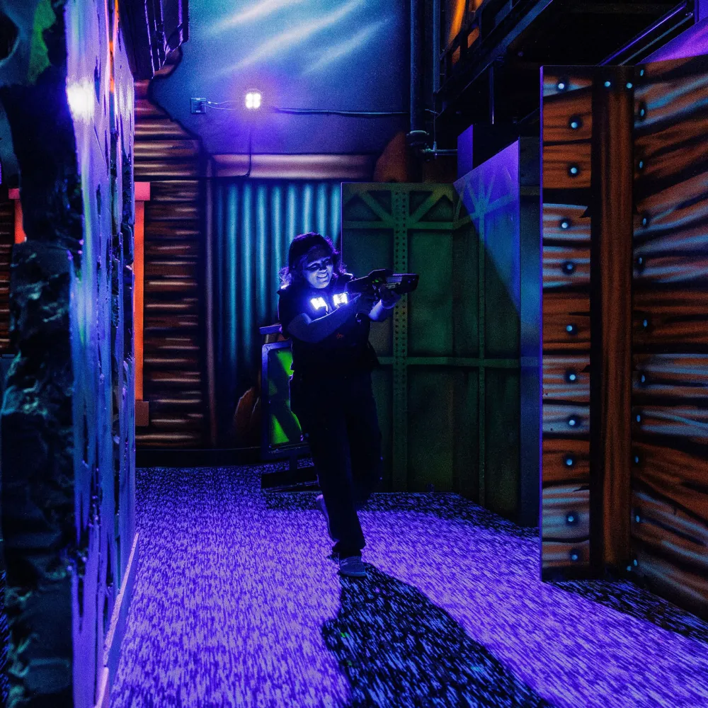 Person playing laser tag in dark arena with glowing equipment and neon-lit walls and floors