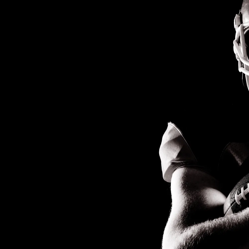 Silhouetted American football player holding ball against dark background with dramatic lighting