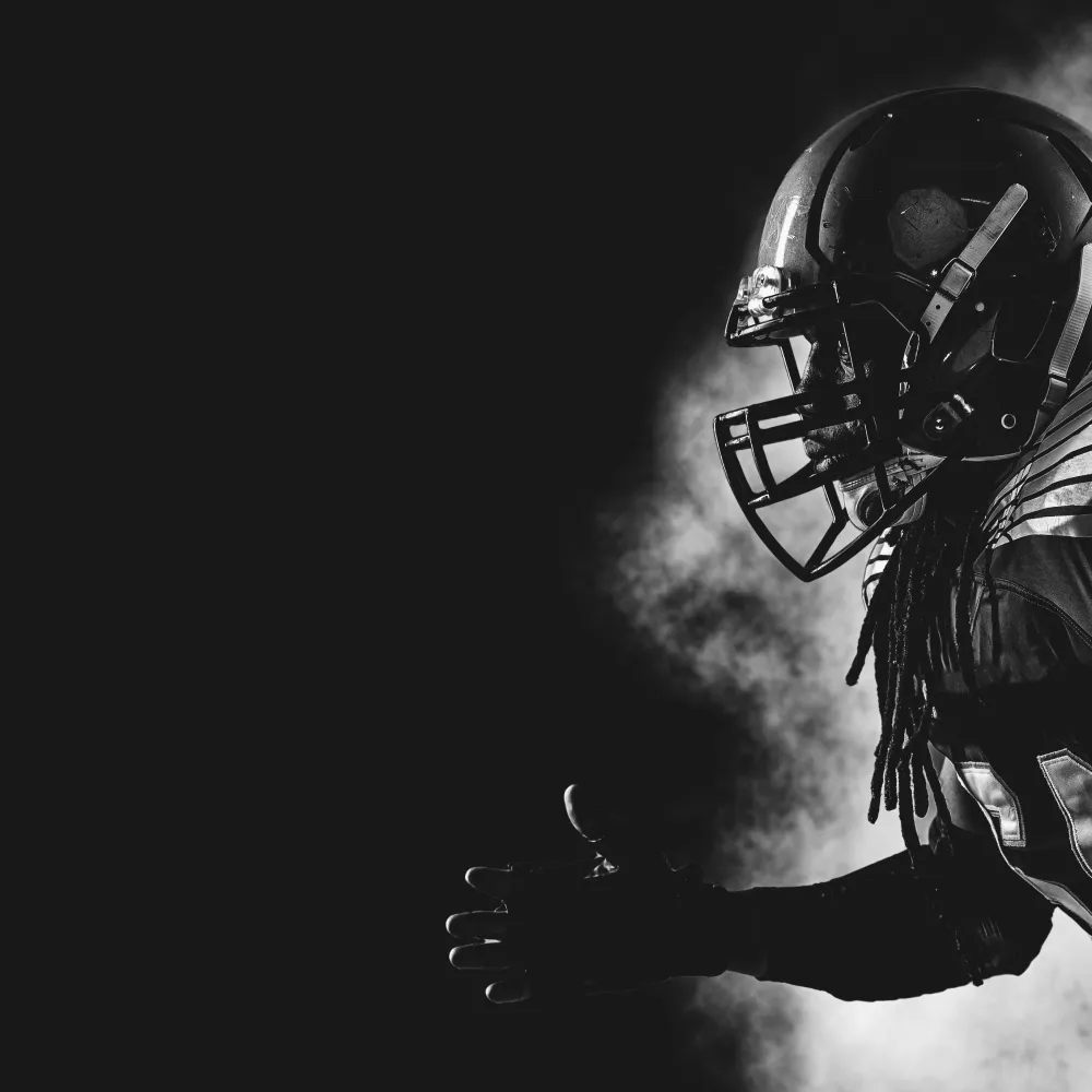 Black and white photo of an American football player in full gear running in profile with smoke behind him
