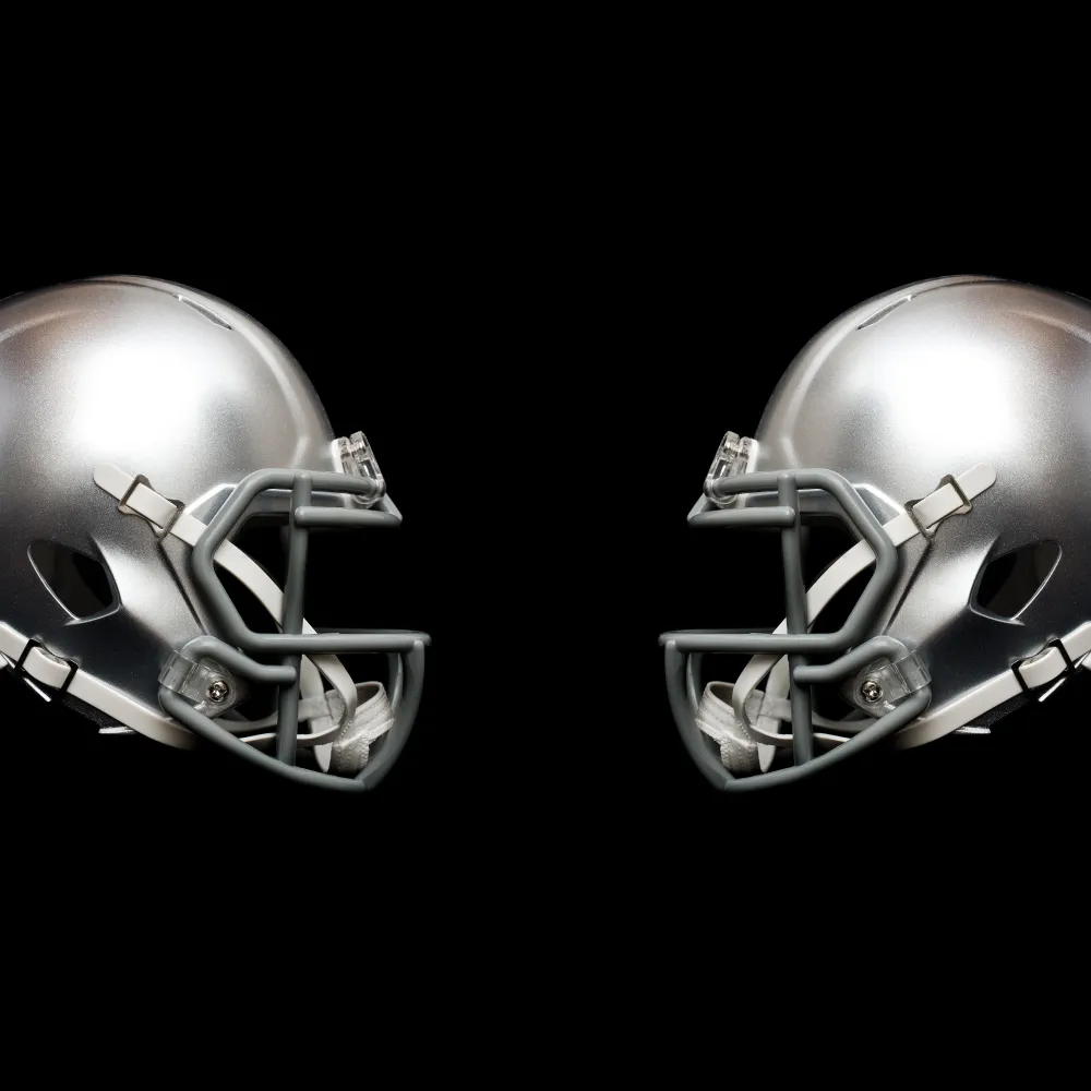 Two silver football helmets facing each other on a black background highlighting their design and structure